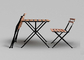 1つのテーブルおよび2脚の椅子は屋外の庭の木製の上の金属フレームの折りたたみを置いた